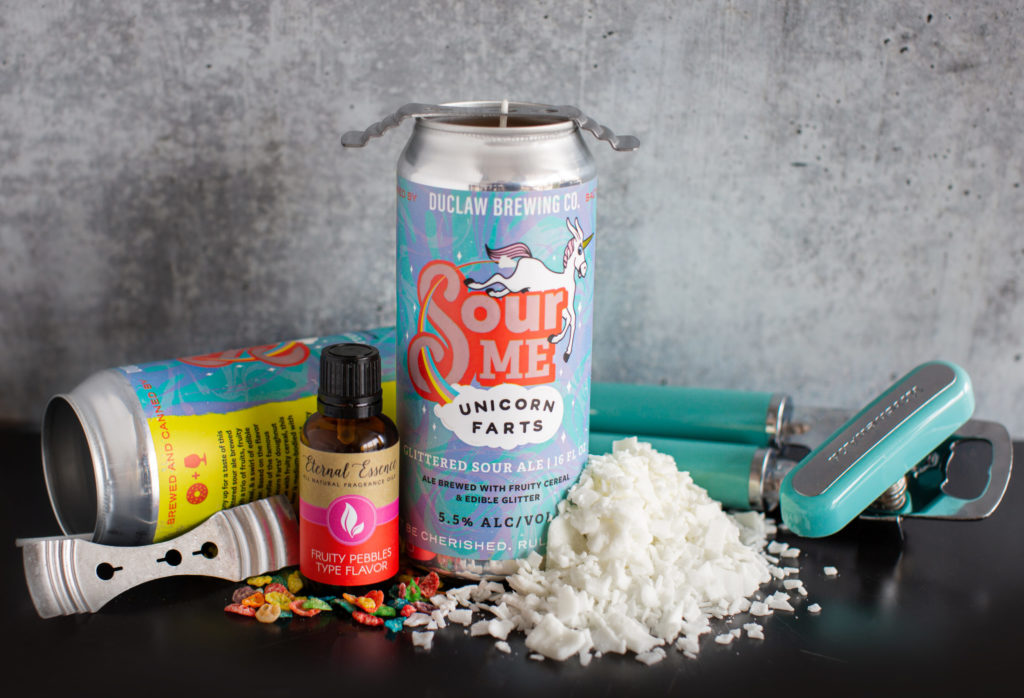Image of Unicorn Farts beer can candle with ingredients surrounding it: can opener, soy wax flakes, wick holder, fruity pebbles fragrance oil, and fruity cereal pieces.